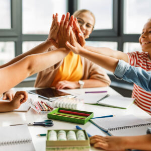 happy students celebrate success around table in classroom.