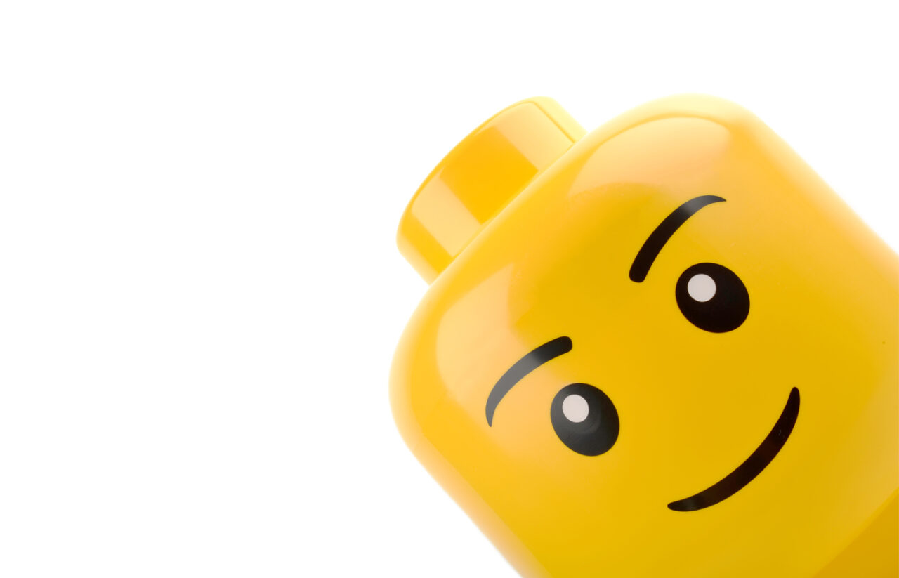 Close-up of a classic yellow LEGO minifigure head with a simple smiling face, representing the timeless design elements that have remained consistent as the LEGO brand has expanded into new products and experiences.